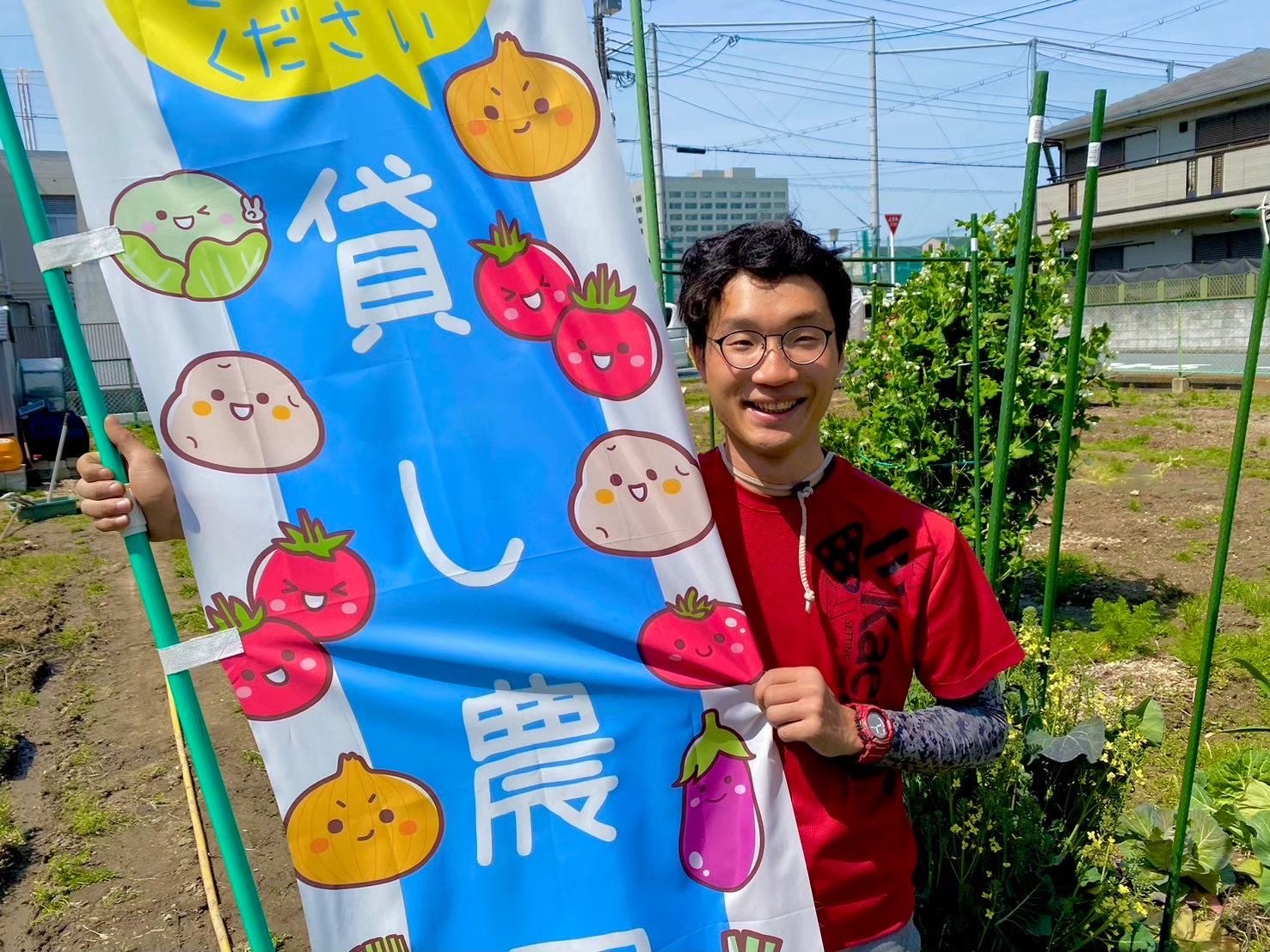 「貸し農園」ののぼりを持って笑う、農園主の上田さん